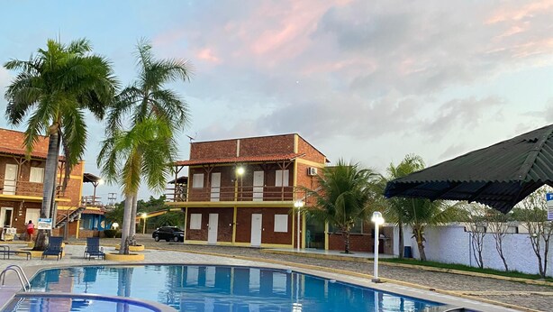 Piscina com superfície de água azul cristalina, rodeada por palmeiras e um edifício com varandas múltiplas.