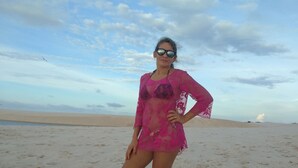 Uma pessoa em pé numa praia de areia, com céu claro e nuvens.