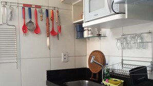 Cozinha moderna com bancada preta, pia de aço inoxidável e fogão a gás. Há um micro-ondas sobre a bancada, e vários utensílios de cozinha pendurados na parede.