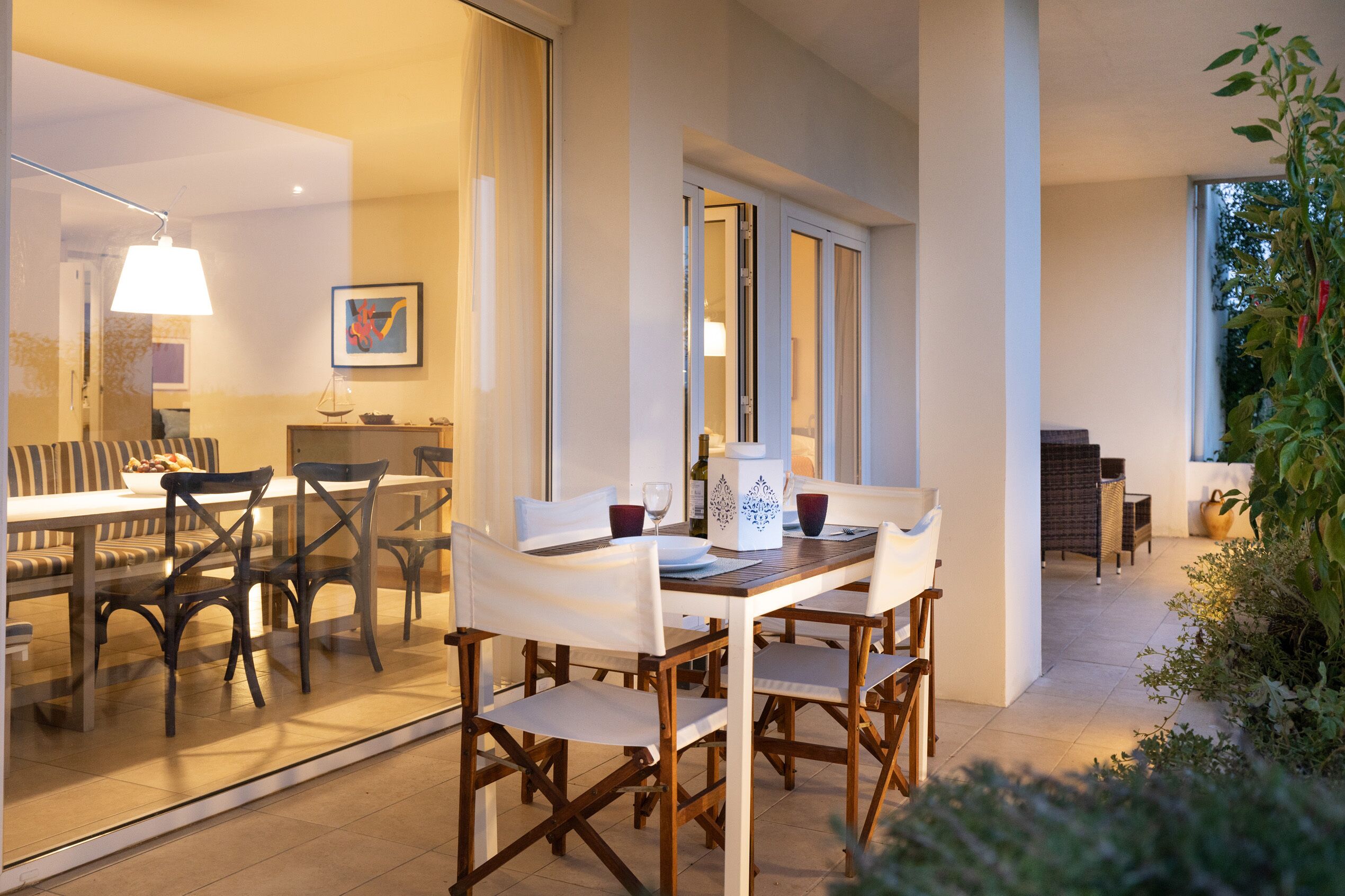 A dining area with a table set for four, surrounded by chairs, and a view of a living room with a sofa and a plant.