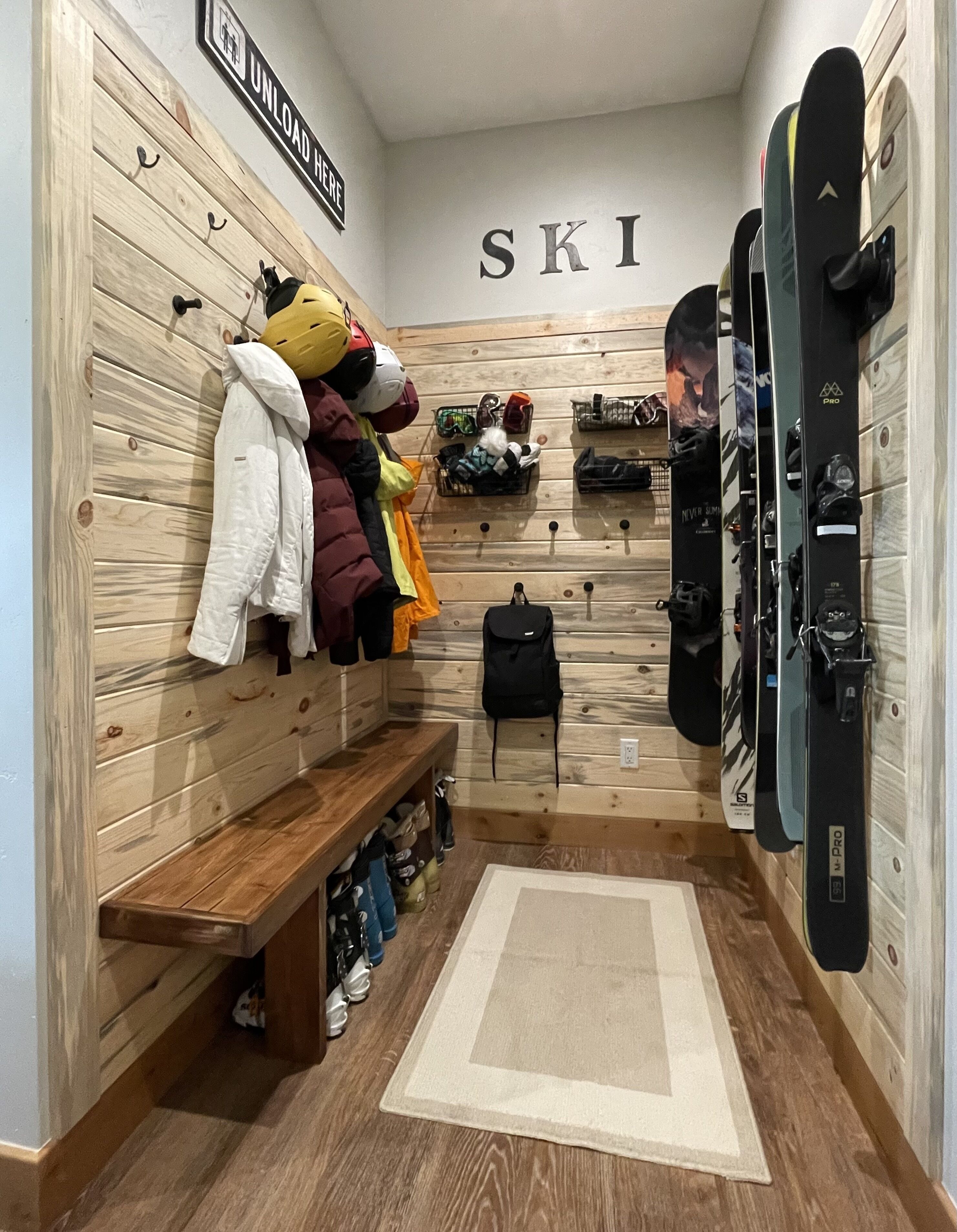 Un espace de rangement pour les skis, équipé de casiers en bois, d’un banc et d’un porte-skis fixé au mur.
