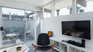 Un salon moderne doté d’un grand téléviseur, de sièges confortables et d’une porte vitrée donnant sur un espace extérieur.