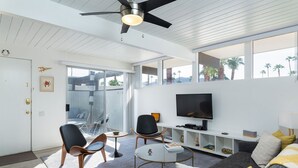 Un salon moderne doté d’un téléviseur à écran plat, de sièges confortables et d’un balcon offrant une vue sur les palmiers.