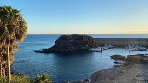Une île rocheuse où des bateaux sont amarrés à un quai situé à proximité, entourée d’une mer calme et de palmiers.