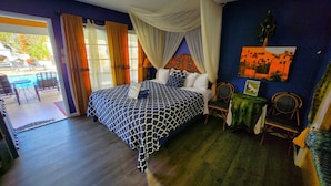 A bedroom with a bed, a chair, a table, and a view of the outside.