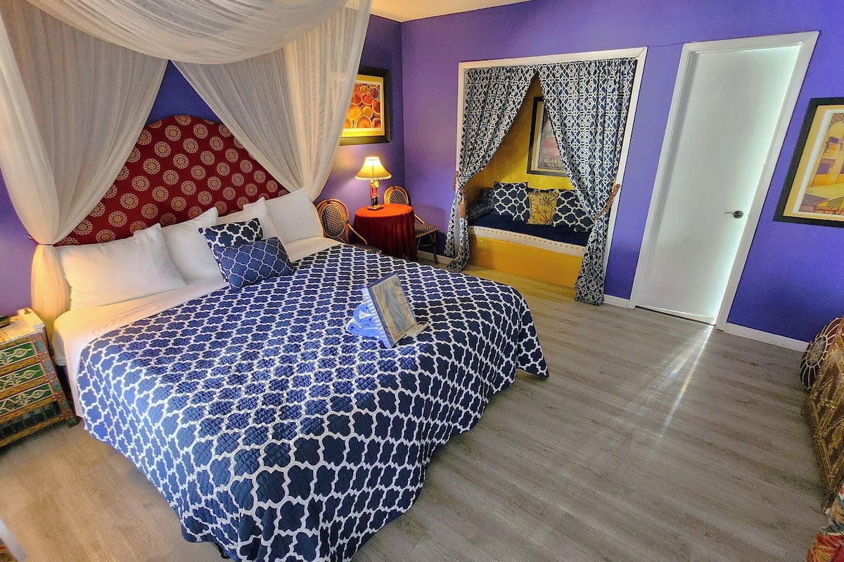 Ein Schlafzimmer mit einem Bett, einem Nachttisch, einer Lampe, einem Sessel, einem Kleiderschrank und einer Tür.