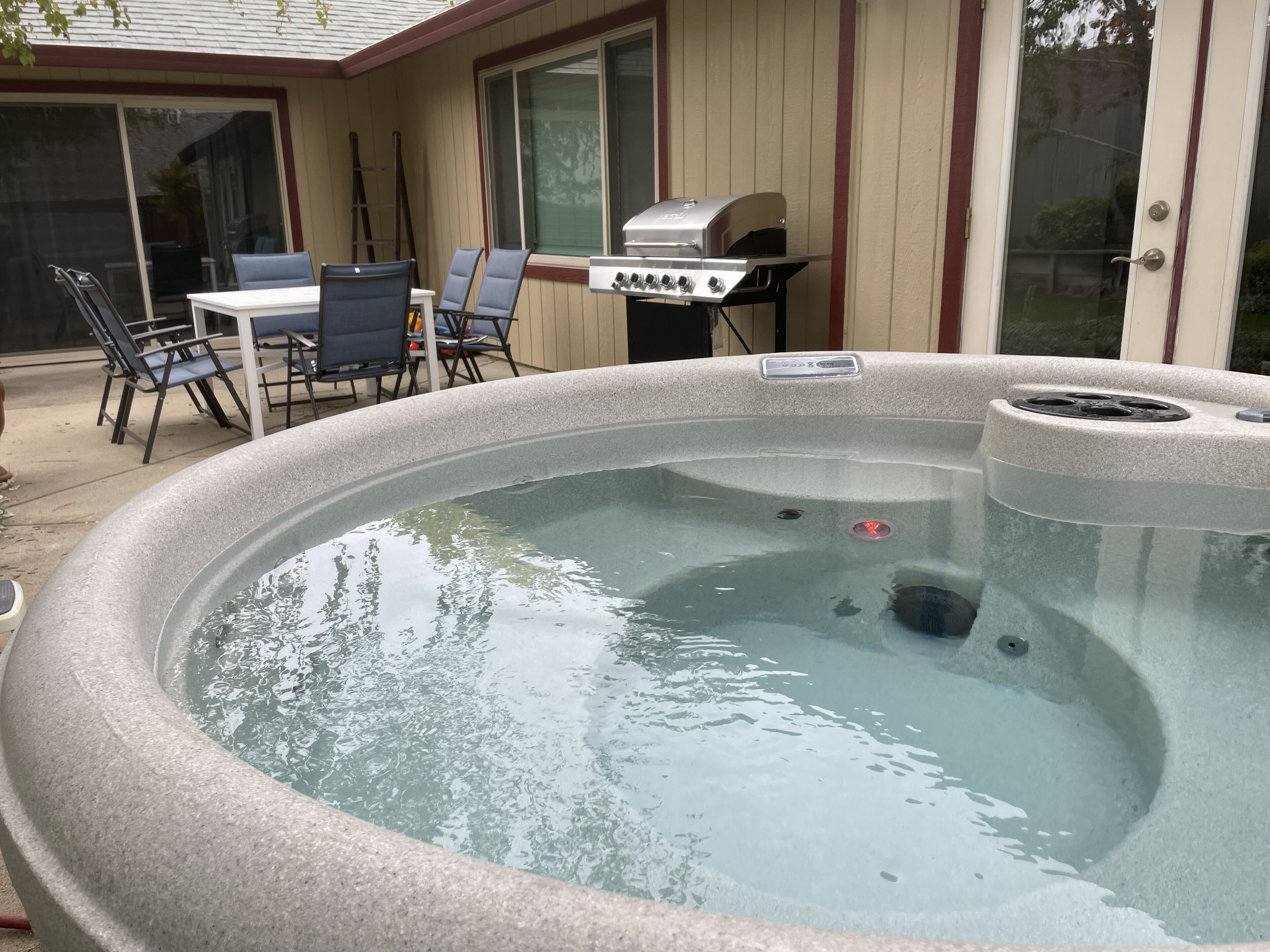 A hot tub with a stone exterior, a barbecue grill, and outdoor seating with chairs and a table.
