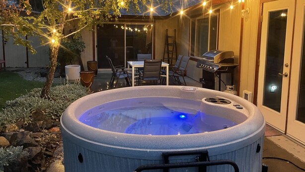 A hot tub with a ladder, a grill, and string lights in a backyard.