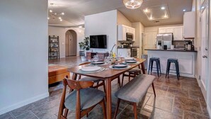 A modern kitchen with white cabinets, a central island, and a dining area with a wooden table and chairs.