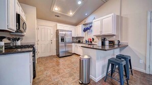 A modern kitchen with white cabinets, a stainless steel refrigerator, a built-in oven, and a stainless steel trash can.