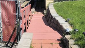 Un chemin menant à une maison dont la façade est bordée de briques rouges et qui est surmontée d’un mur de soutènement en pierre.