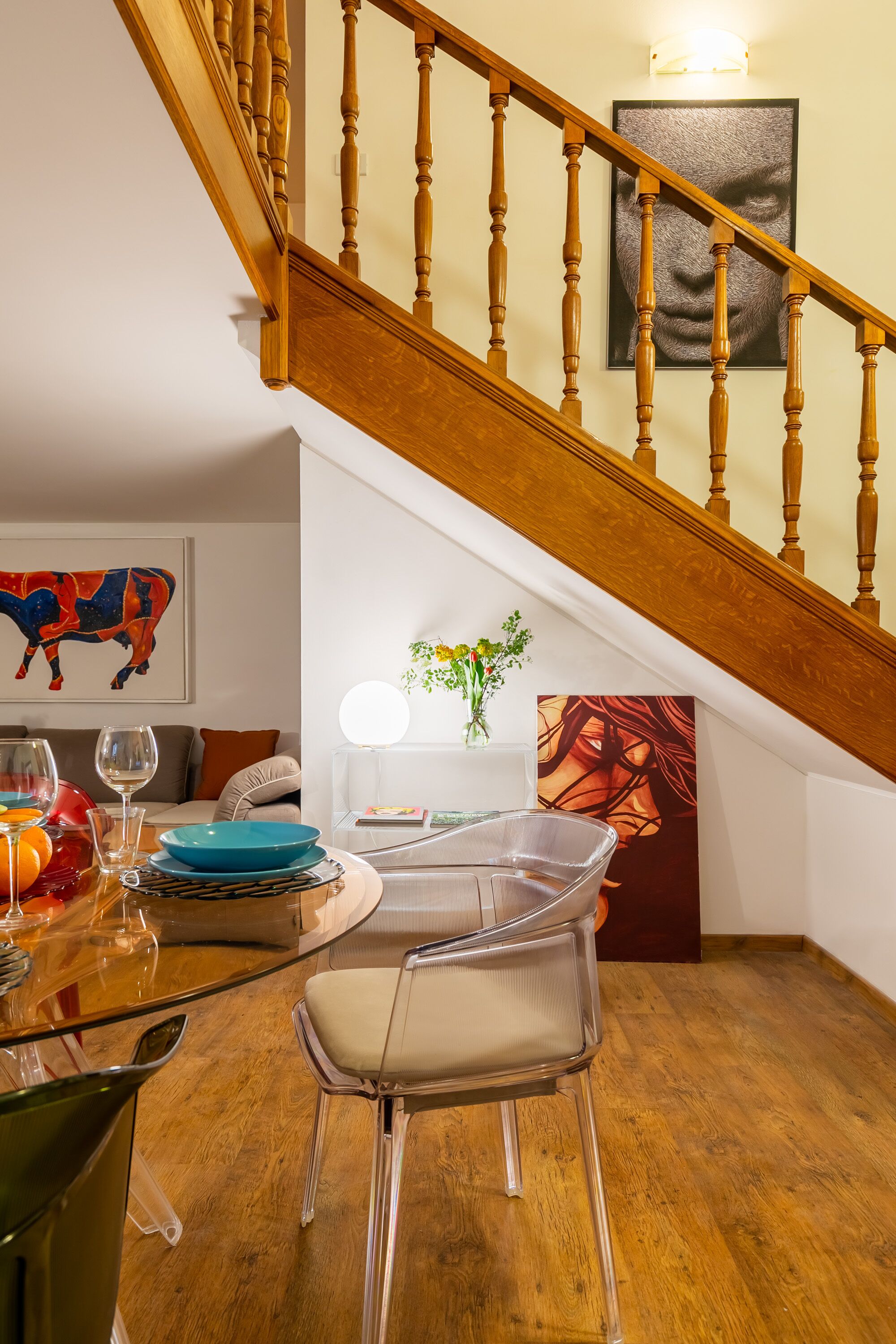 A dining area with a wooden staircase, a clear glass table, and modern chairs.