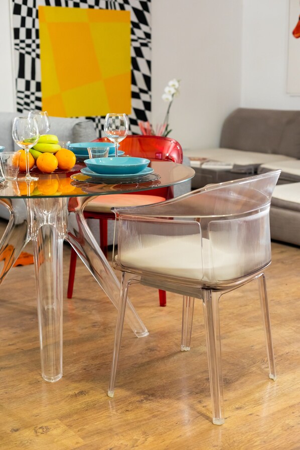 A dining area with a glass table, clear chairs, and a fruit bowl.