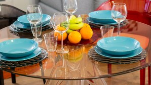 Un tavolo da pranzo con piatti blu, bicchieri trasparenti e un centrotavola di frutta.