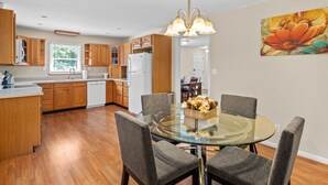 A modern kitchen with wooden cabinets, a white refrigerator, and a dining area with a glass table and four chairs. - WHOLE Home with BASEMENT on 3 Acres (Kennesaw)