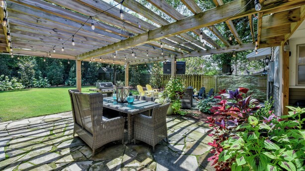 A covered patio with a stone floor, wicker furniture, and potted plants.