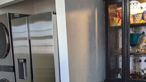 A kitchen with a black and white checkered floor, a stainless steel refrigerator, a washing machine, and a dark wooden cabinet with glass doors. - Escape to Wonderland (Oklahoma City)