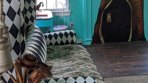 A room with a large tree mural on the wall, a checkered sofa, and a window with blinds. - Escape to Wonderland (Oklahoma City)