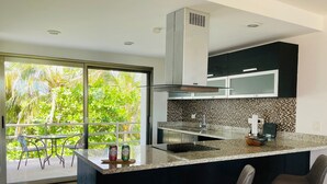 A modern kitchen with a large island, black cabinets, and a view of lush greenery through the sliding doors. - Paraiso304; Entire Luxury Condo 3 minute walk from the beach (Playa Paraíso)