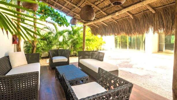 A covered outdoor seating area with wicker furniture and a thatched roof. - Paraiso304; Entire Luxury Condo 3 minute walk from the beach (Playa Paraíso)