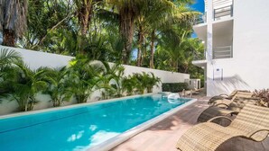 A swimming pool with lounge chairs, surrounded by lush greenery and a white building. - Paraiso304; Entire Luxury Condo 3 minute walk from the beach (Playa Paraíso)