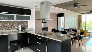A modern kitchen with dark cabinetry, a stainless steel range hood, and a marble countertop. - Paraiso304; Entire Luxury Condo 3 minute walk from the beach (Playa Paraíso)