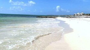 A beach with clear water, a sandy shore, and a distant building. - Paraiso304; Entire Luxury Condo 3 minute walk from the beach (Playa Paraíso)