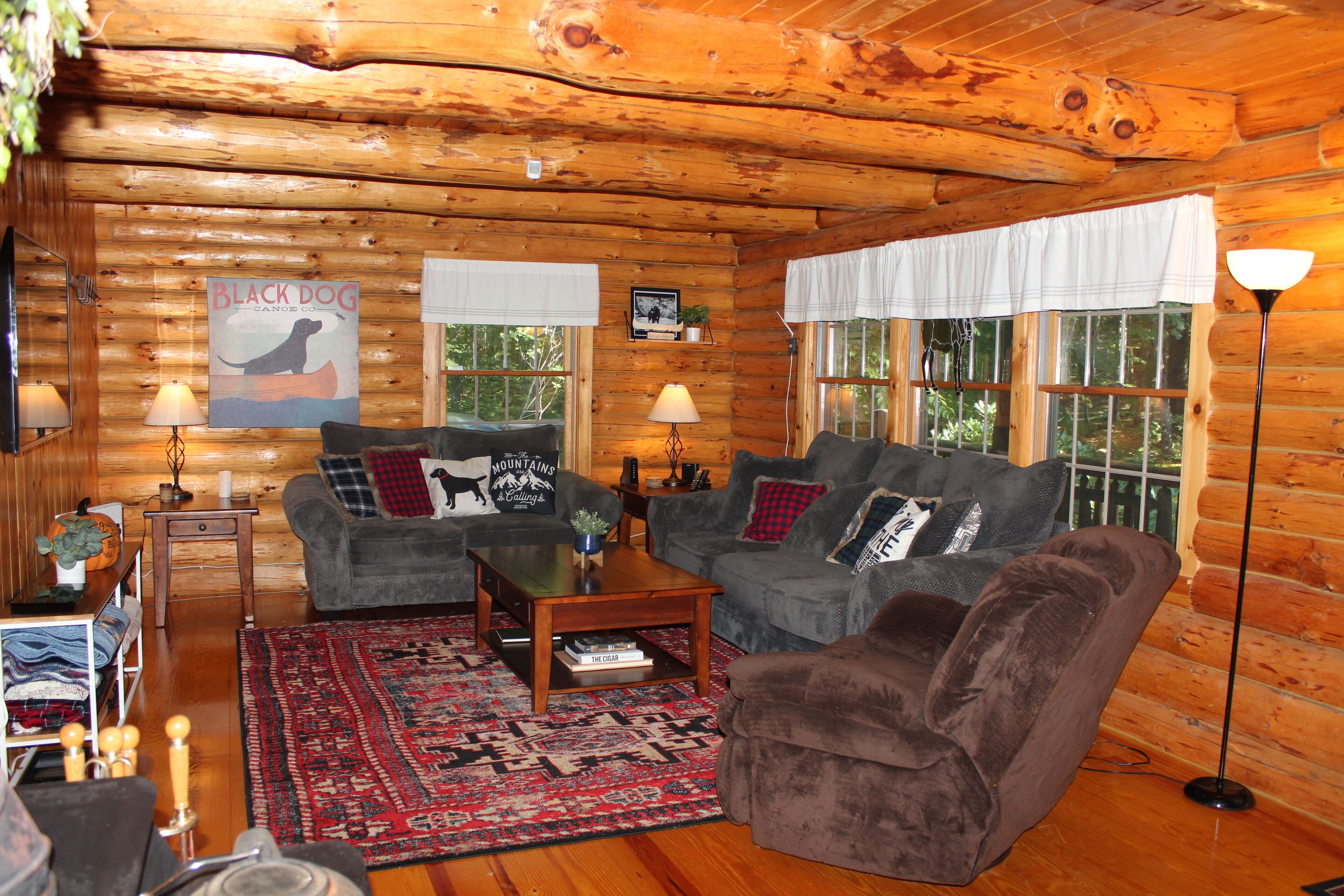 Ein gemütliches Blockhaus-Interieur mit zwei grauen Sofas, einem Couchtisch und einem gemusterten Teppich.
