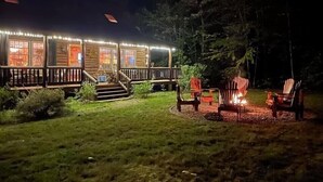 Uma cabana de registos com um alpendre, área de estar exterior e lareira.