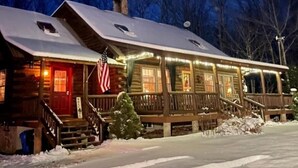 Uma cabana de troncos com varanda, bandeira americana e luzes de Natal.