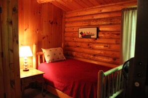 A wooden cabin room with a bed, a nightstand with a lamp, and a framed picture on the wall. - Dog-Friendly 5 Bedroom Log Cabin with Hot Tub in the Heart of Southern Maine  (Brownfield)