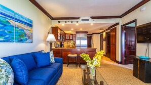 A living room with a blue sofa, a coffee table, and a kitchen in the background. - Waipouli Beach Resort Exquisite Ocean View Condo in Oceanfront H Building! (Kapaa)