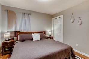 Un dormitorio con cama, mesitas de noche, lámpara, reloj, puerta e iluminación en la pared.