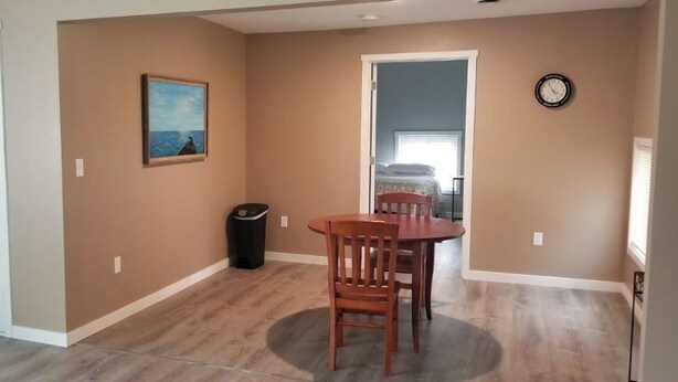 Un coin repas avec une table et des chaises, un tableau au mur, une poubelle et une porte.