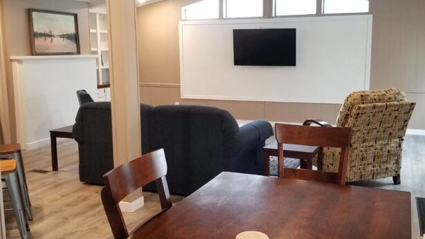 Un comedor con mesa y sillas de madera, un sofá negro y un sillón estampado.