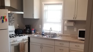 Una cocina moderna con armarios blancos, encimera de madera, cocina a gas y dos taburetes.