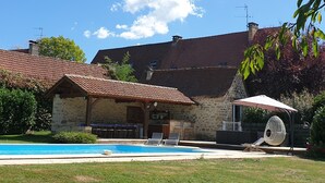 A stone house with a swimming pool, outdoor seating, and a hanging chair. - Au Fil des Hirondelles (Bio)