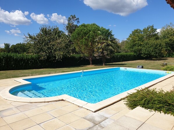 A rectangular swimming pool with a tiled deck, surrounded by a well-maintained lawn and trees.