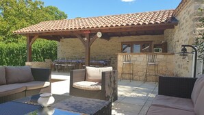An outdoor patio with wicker furniture, a stone wall, and a tiled roof. - Au Fil des Hirondelles (Bio)