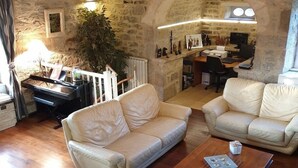 A spacious living area with a stone wall, a wooden coffee table, and two white leather sofas. - Au Fil des Hirondelles (Bio)