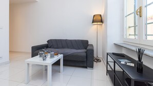 A modern living room with a grey sofa, a white coffee table, a floor lamp, and a small black TV stand.