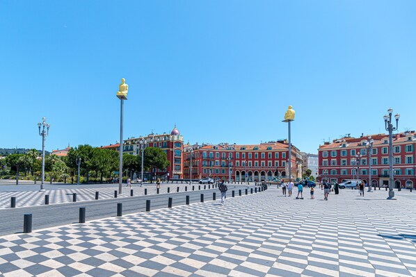 A public square with a checkered pavement, a statue, and red buildings in the background.