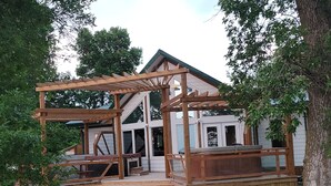 A wooden deck with a fire pit, a covered outdoor seating area, and a house with a gabled roof and large windows.