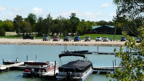 A marina with boats docked, a parking area with cars, and a building in the background.