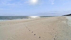 Une vaste plage de sable où l’on peut voir des empreintes de pas menant à l’eau, un ciel dégagé et un soleil éclatant.