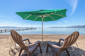 A beach scene with two chairs and a green umbrella, a pier in the background, and a clear sky. - Beautifully updated 3 bedroom townhome in The Northshore complex (Tahoe City)
