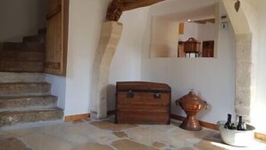 A stone-floored hallway with a wooden staircase, a wooden chest, and a copper pot on a table. - Cozy Cottage (Éméville)