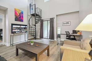 Un salon moderne avec un escalier en colimaçon, un téléviseur à écran plat, une table basse et un canapé.