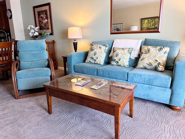 A living room with a blue sofa, two armchairs, a glass coffee table, a lamp, and a painting on the wall.