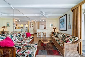 A living room with a sofa set, a dining area, and a kitchen in the background.